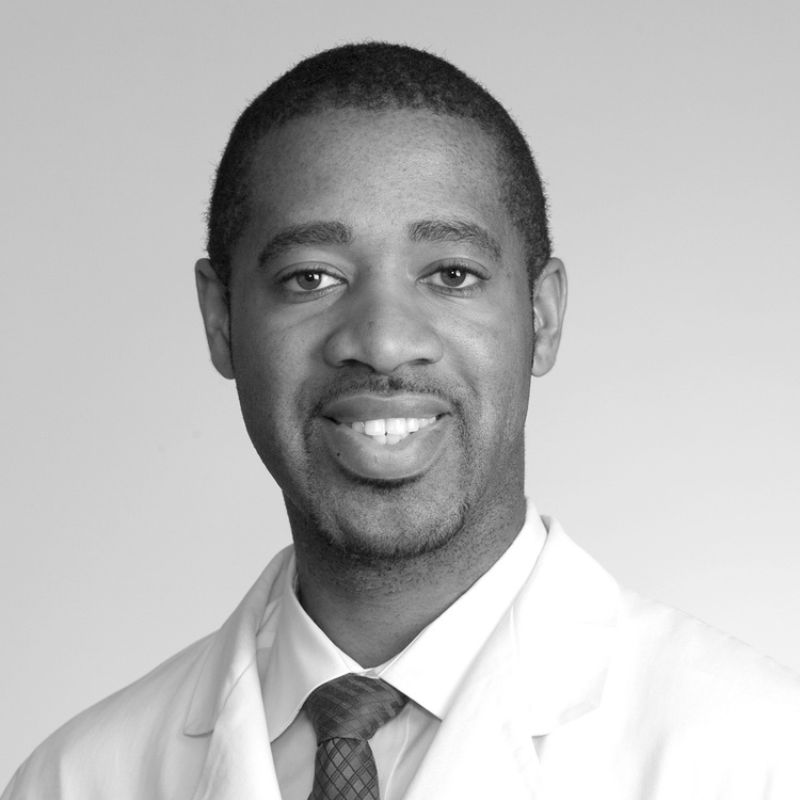 Dr. Ike Iheagwara, audiologist, smiling in a white coat and patterned tie (black and white photo)